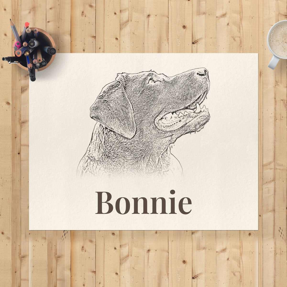 Unframed 30×40cm pencil-style dog portrait print with the name Bonnie, flat lay on a pine desk